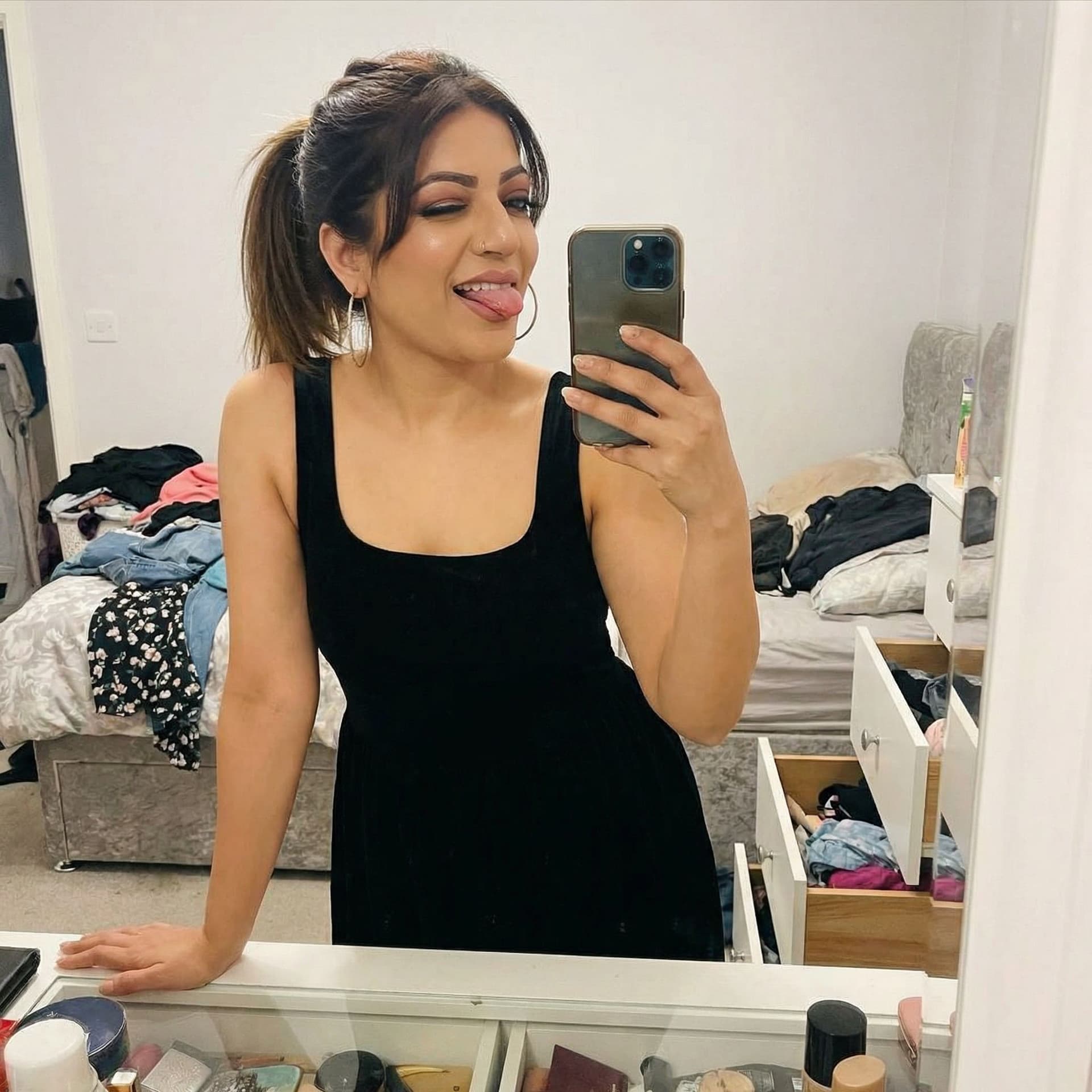 AI generated: takes a mirror selfie in a messy bedroom.

The woman has her phone in one hand and she is using her ...