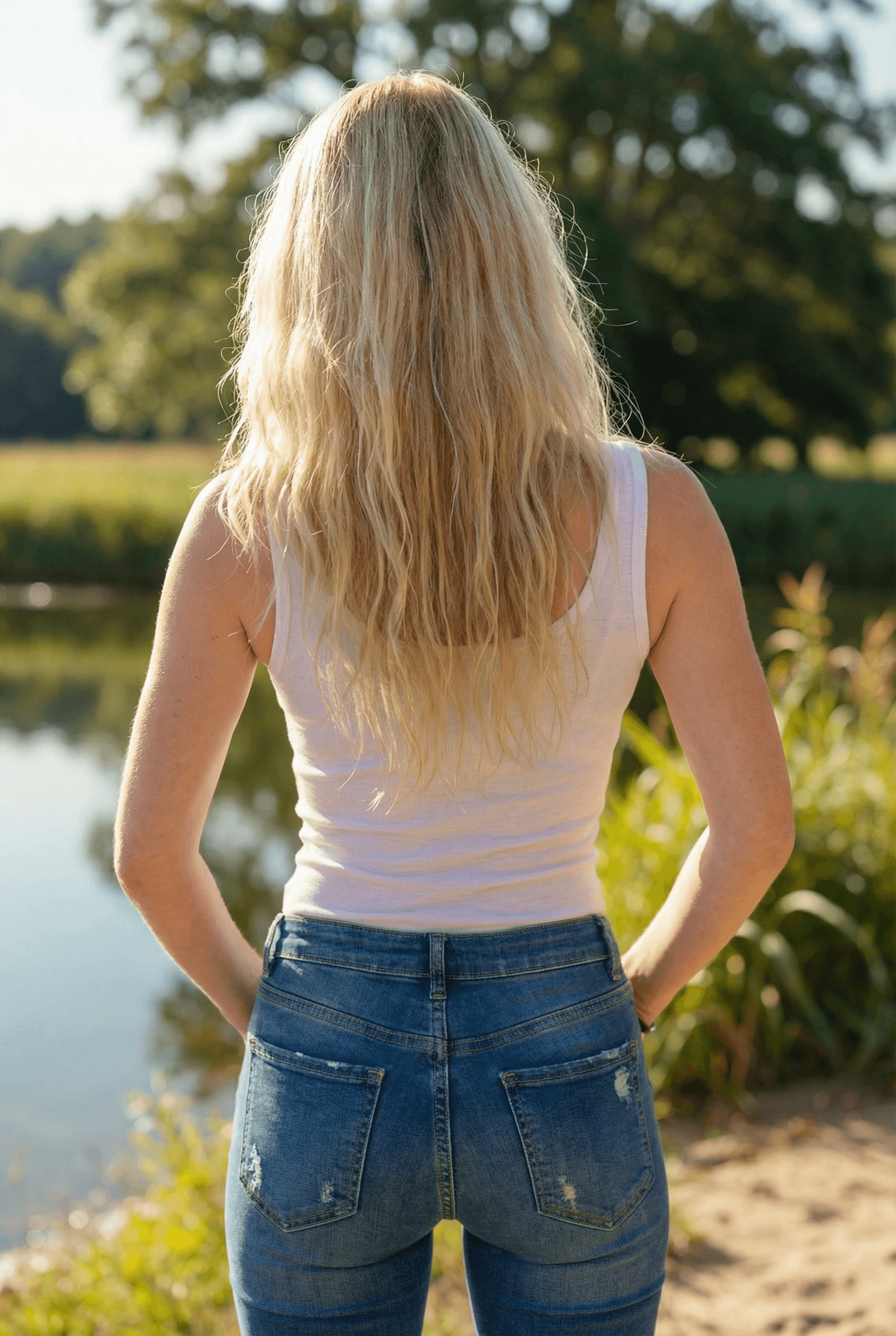 AI generated: A fit adult woman stands in a sunlit outdoor setting, facing the camera, her hands resting casually ...