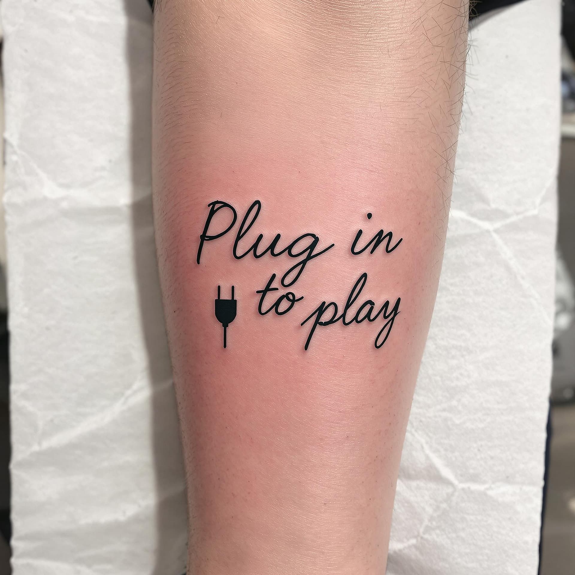 AI generated: a tattoo with the text "Plug in to play"