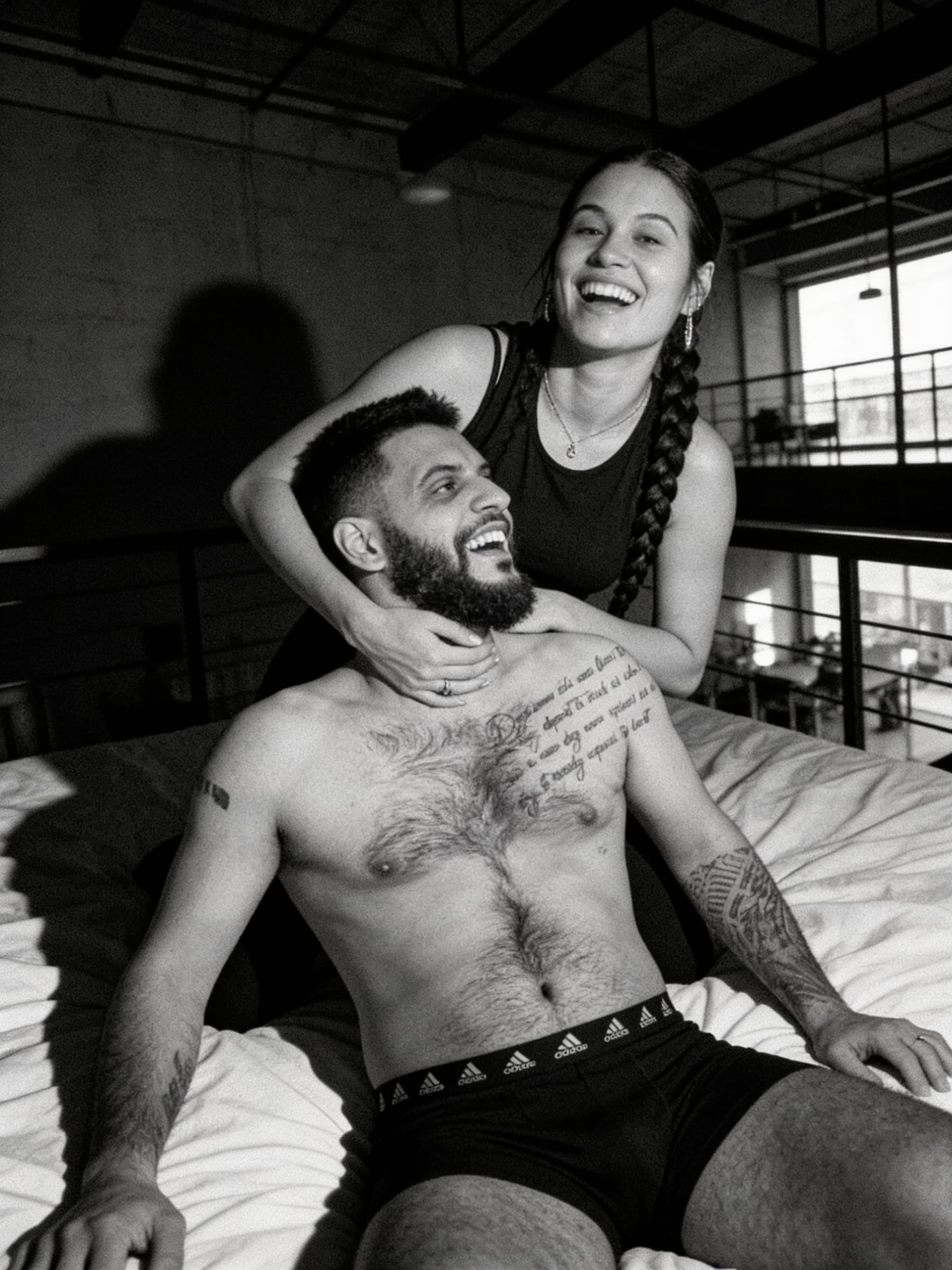 AI generated: A moody, high-contrast photograph of a couple in a modern loft. The woman is positioned playfully ov...