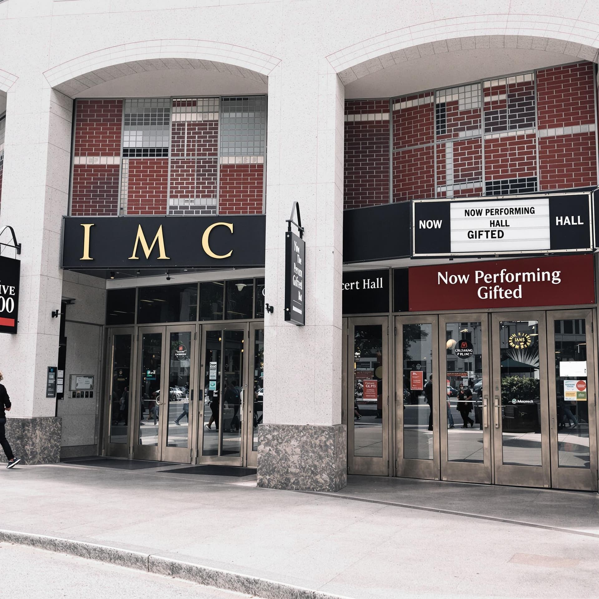 AI generated: outside view of a concert hall with a big sign on the front with writing " Now Performing
Gifted" 