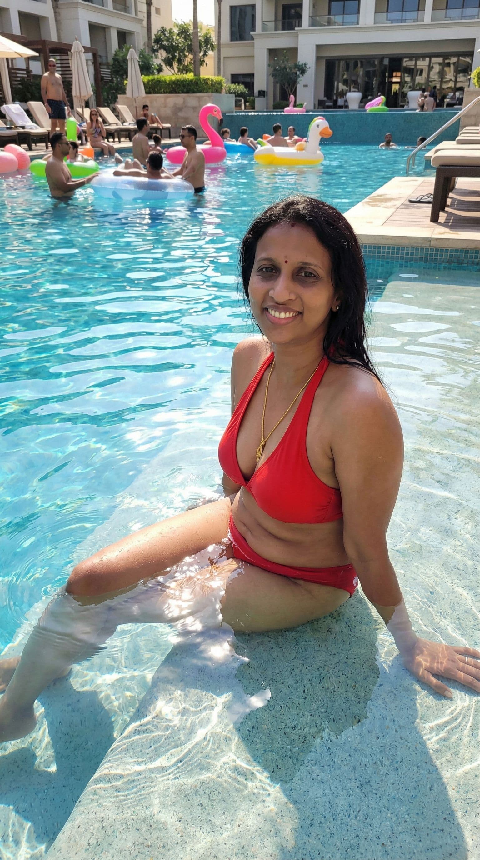 AI generated: a woman in a red bikini sitting on the edge of a pool in the sun, squatting down next to a pool, nex...