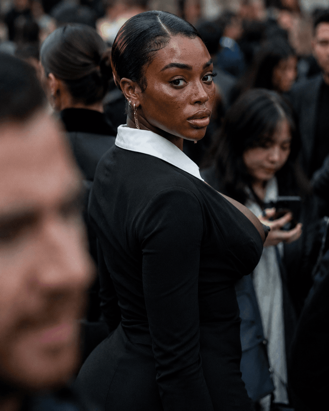 AI generated: candid street-fashion portrait in a dense crowd, subject caught mid-turn while looking back toward t...