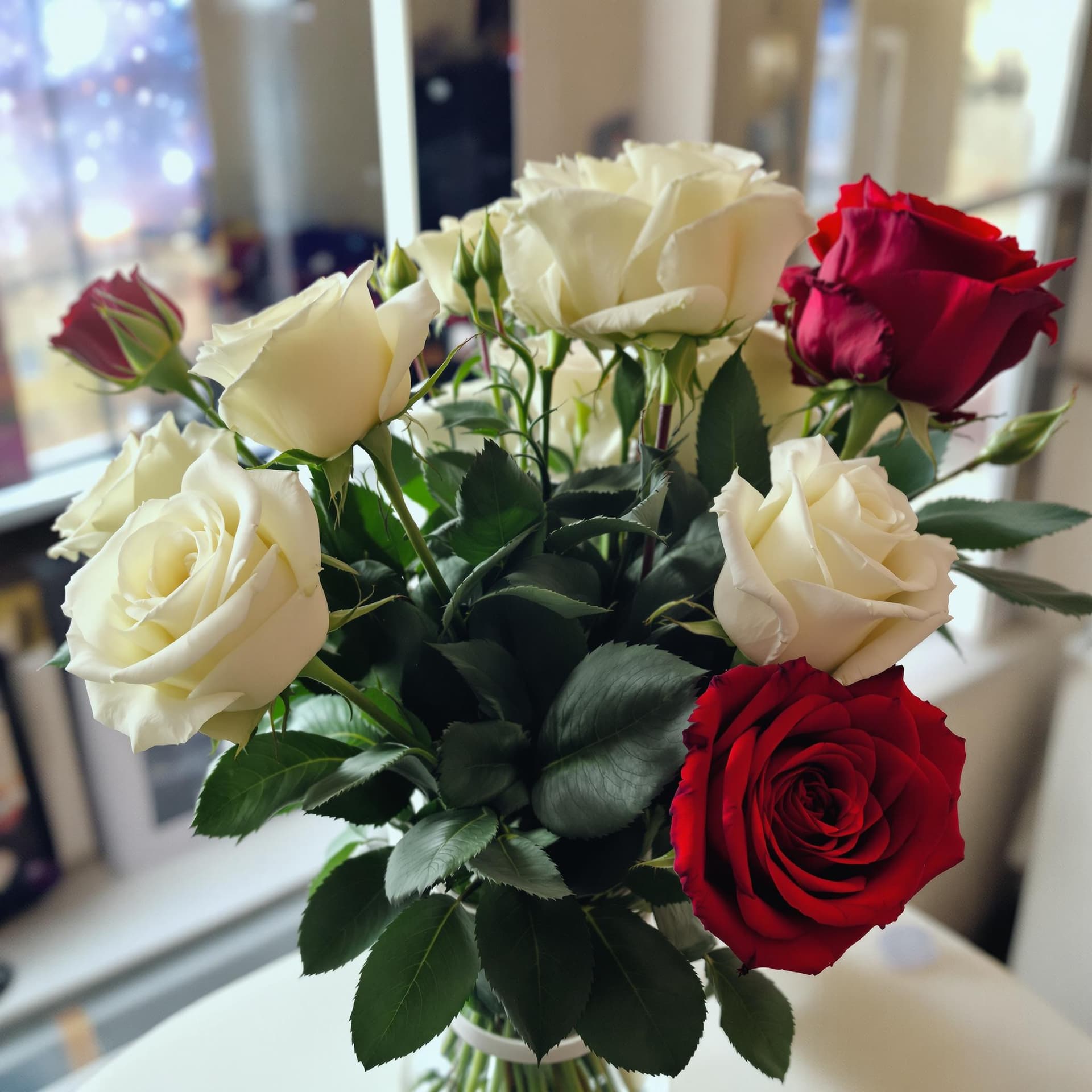 AI generated: A bouquet of white Roses and Red roses in a clear vase on a table with a window that displays the un...