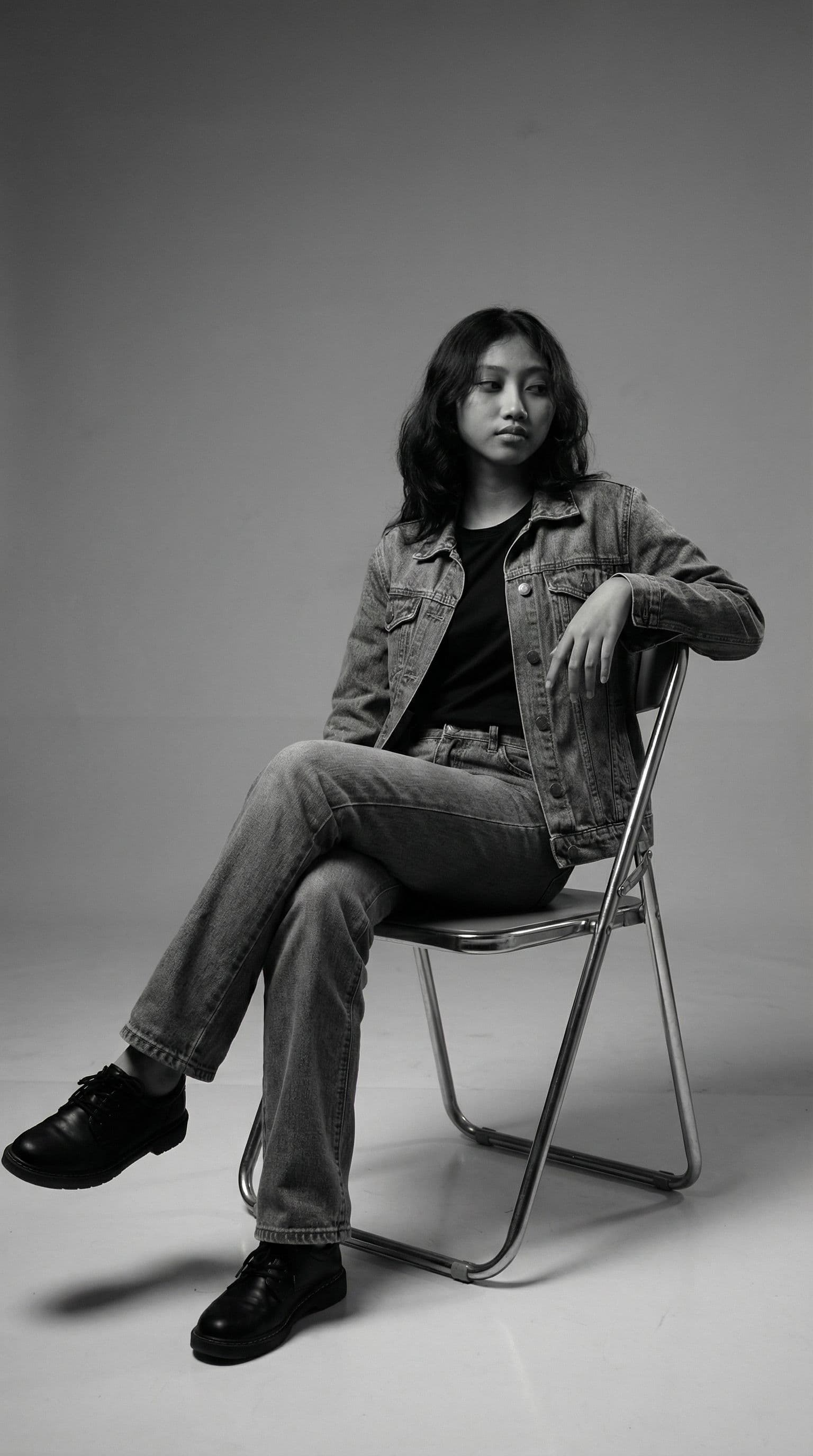 AI generated: Create a black and white studio photo showing me setting casually on a metal folding chair with his ...