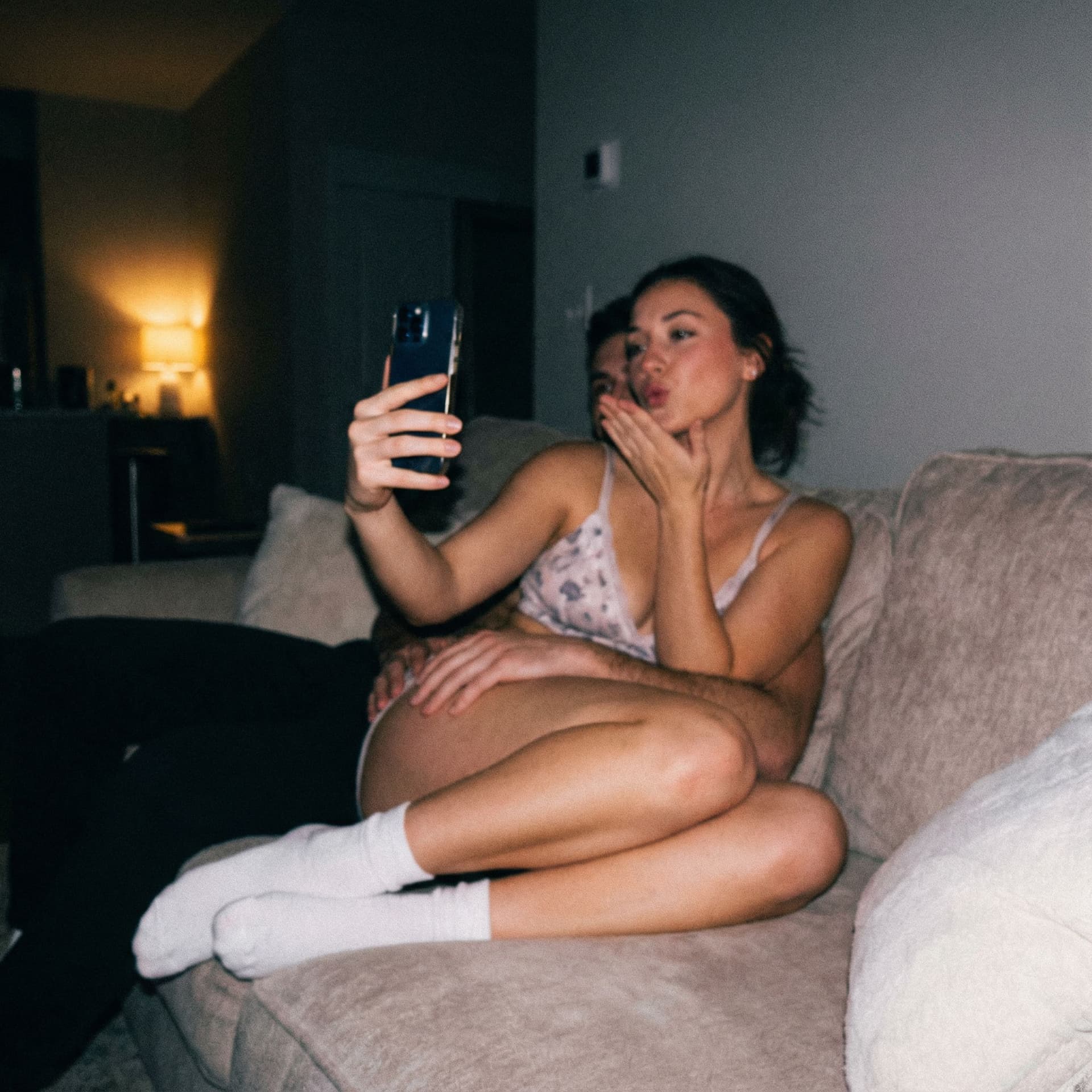 AI generated: Romantic selfie blowing a kiss at me,a sloppy snapshot. Sitting on a couch at night teasing(no light...