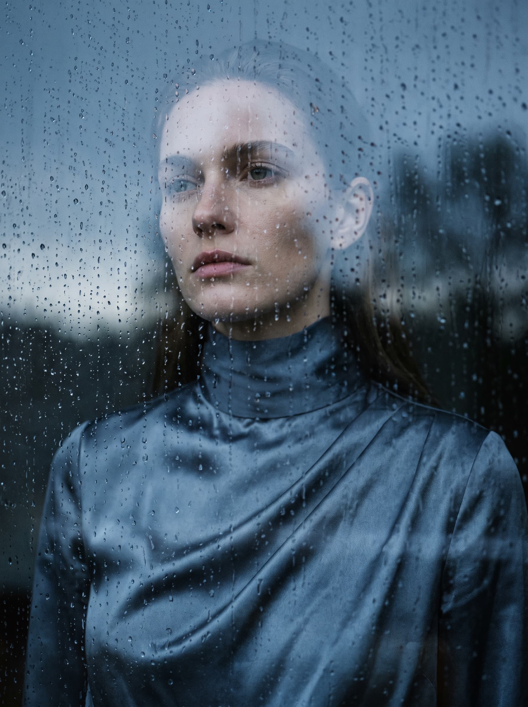 AI generated: (Nano Banana Pro) Close-up fashion photography. A female model viewed through a pane of rain-streake...