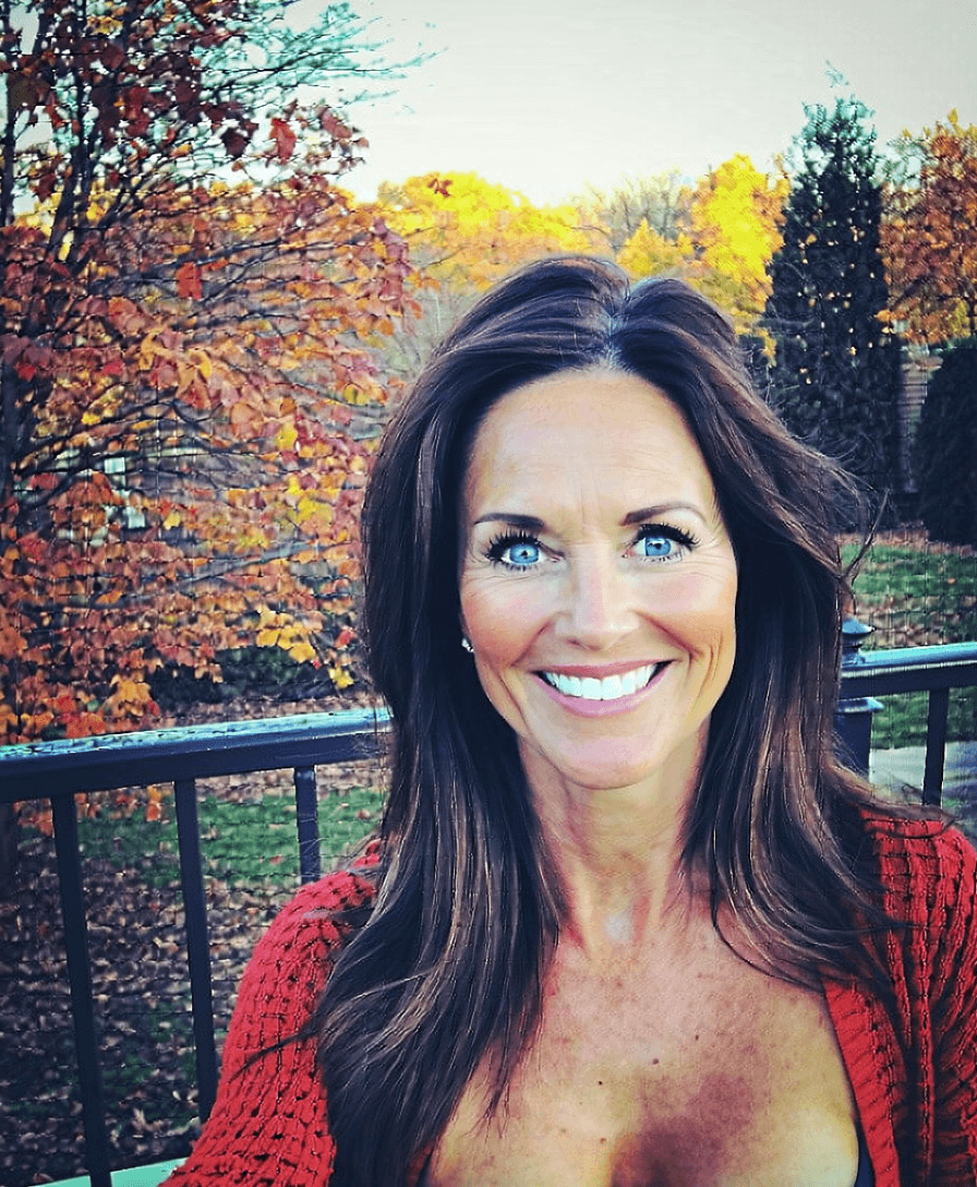 AI generated: A 40-year-old woman with long, dark brown hair and bright blue eyes is smiling in front of a fall ba...