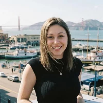 AI generated video: camera position is fixed | slight breeze that makes her hair move | she smiles and kisses at the cam...