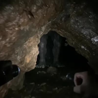 AI generated video: A man cautiously walks into a dark cave, holding a small flashlight that barely illuminates the rock...