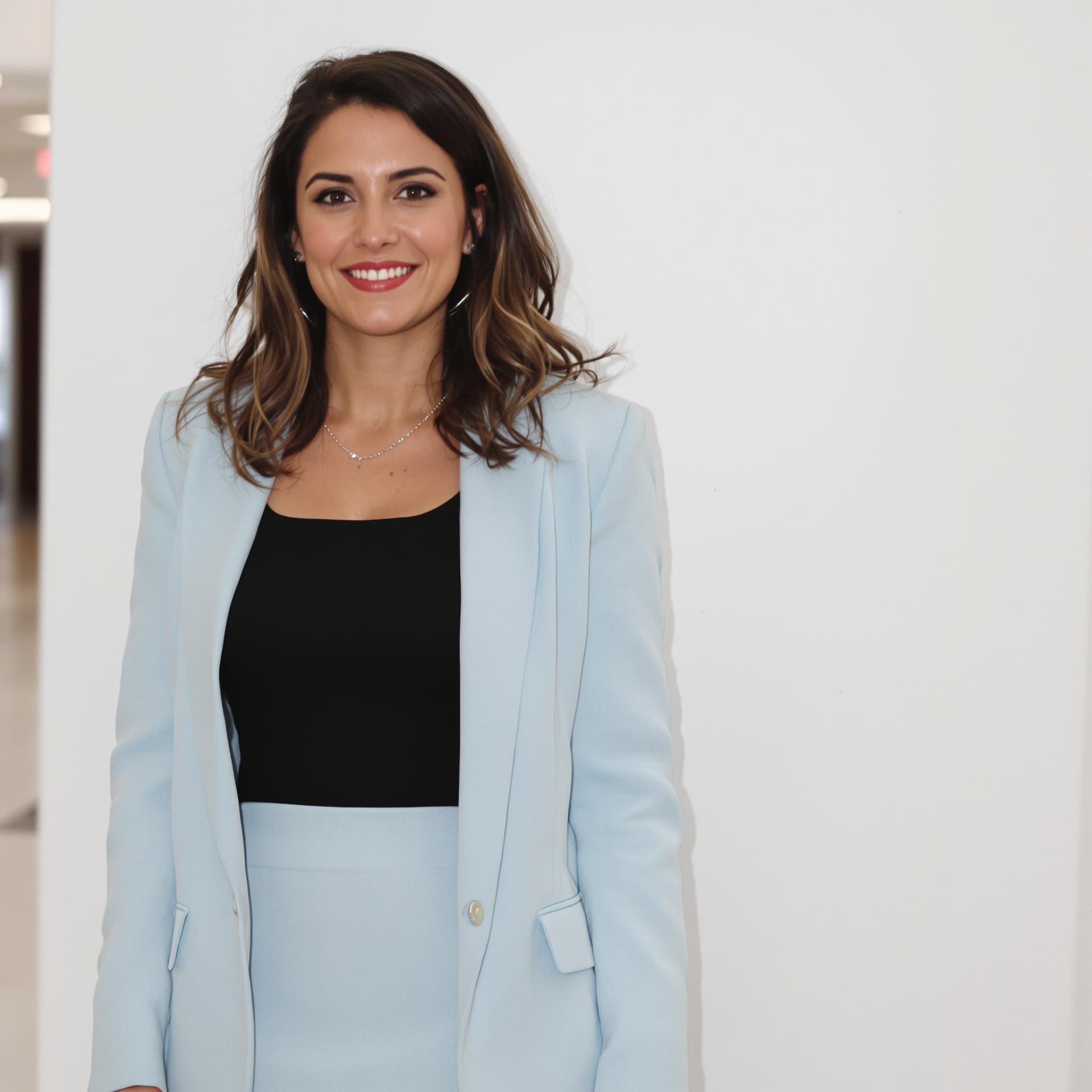 AI generated: woman stands in a hallway. She is dressed in a black top, a light blue blazer, and a skirt. The back...
