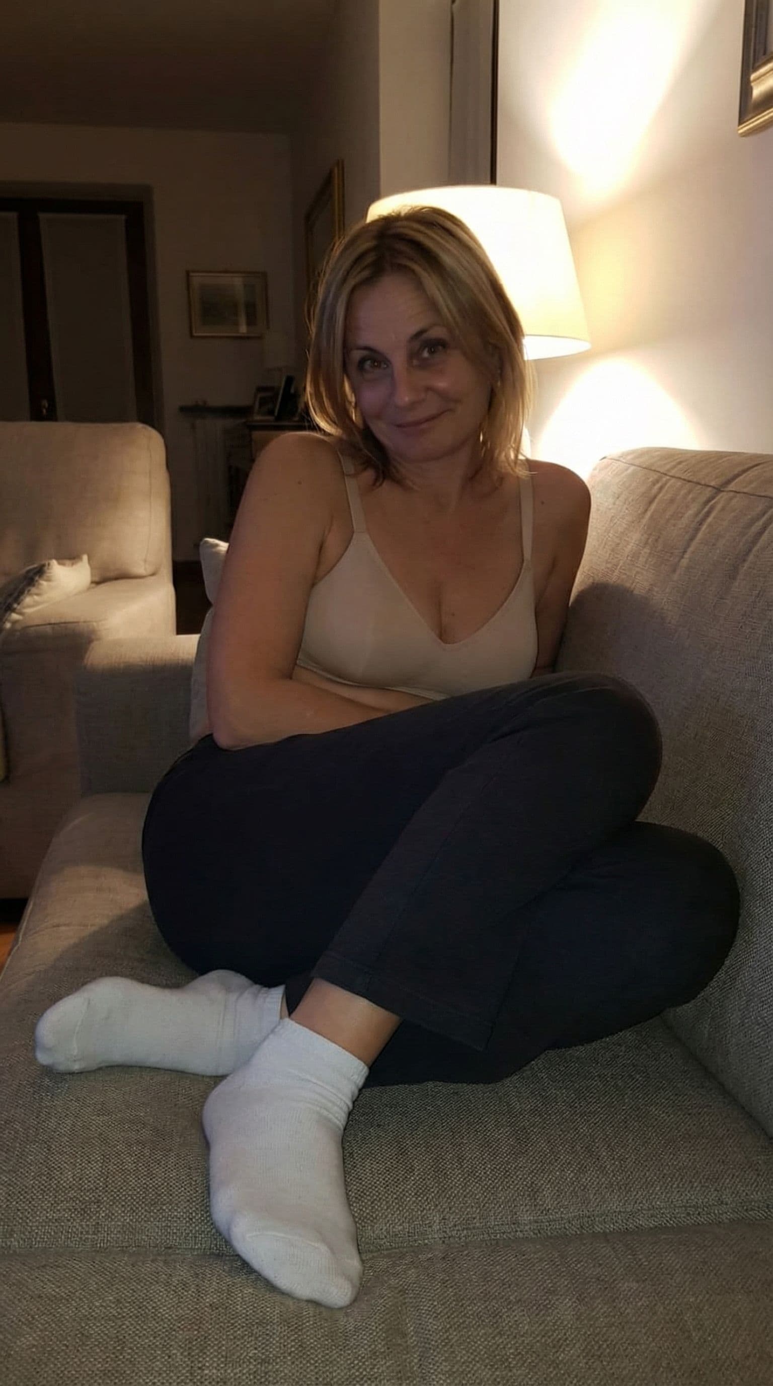 AI generated: looking at me,a sloppy snapshot. Sitting on a couch at night teasing, home bra and white socks