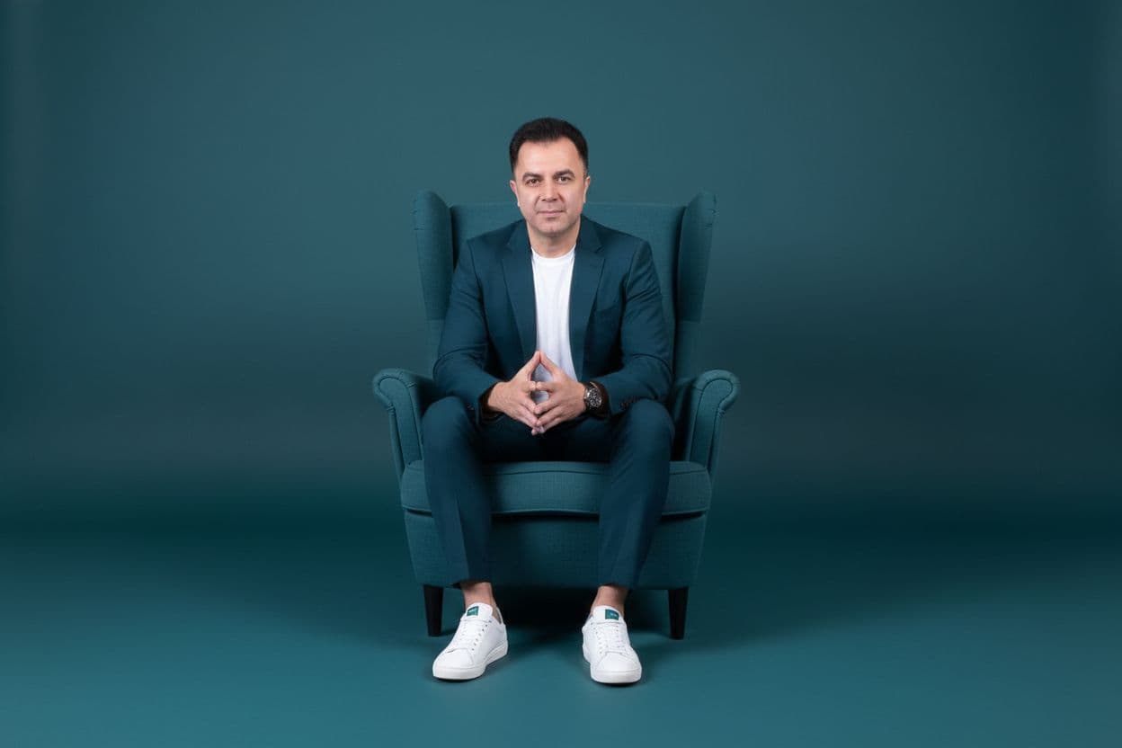 AI generated: Convert this image so that the man is sitting in the center of a high-back armchair in a minimal, mo...