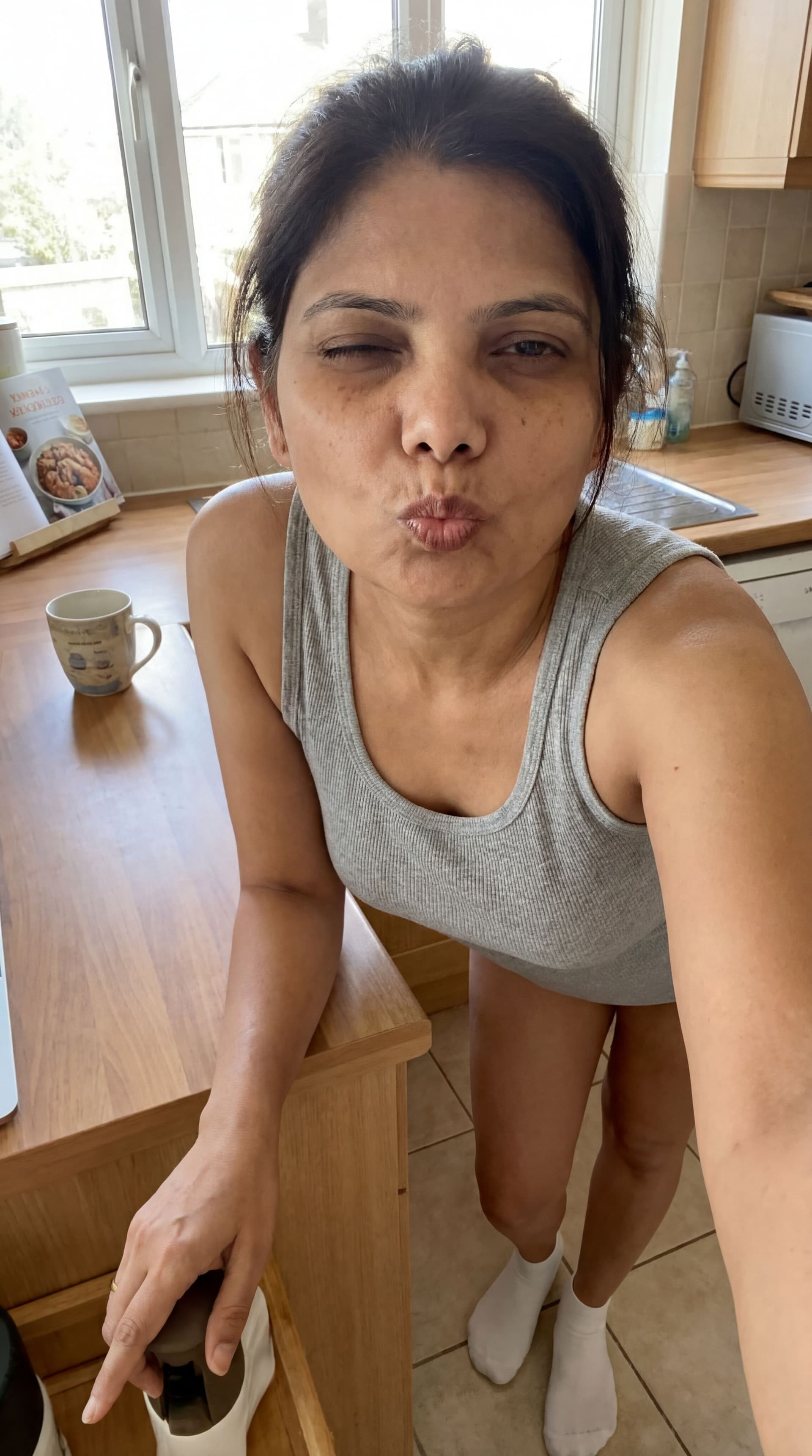 AI generated: Teasing, leans over on a kitchen desk, wearing a tanktop and white socks, sleepy eye contact blowing...