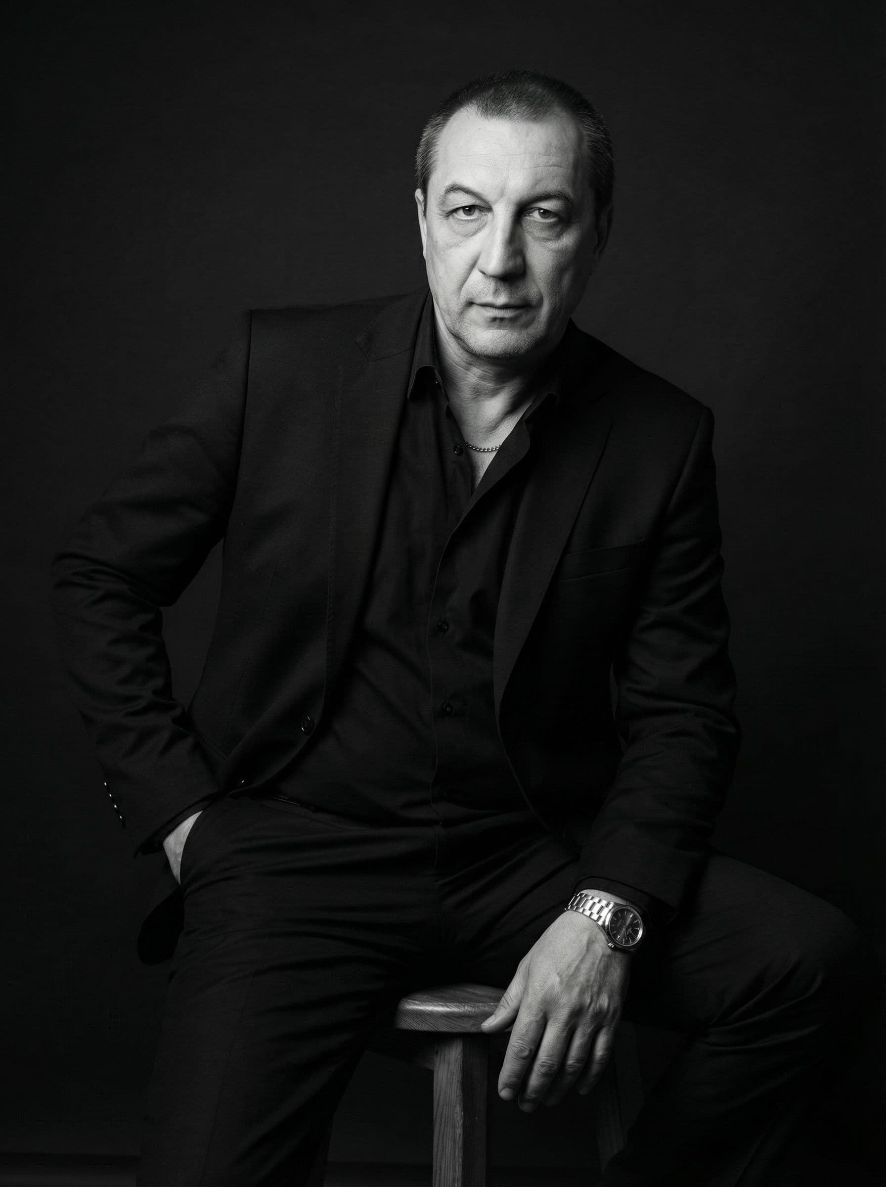 AI generated: A moody studio portrait of a confident man sitting on a wooden stool against a dark background. He i...