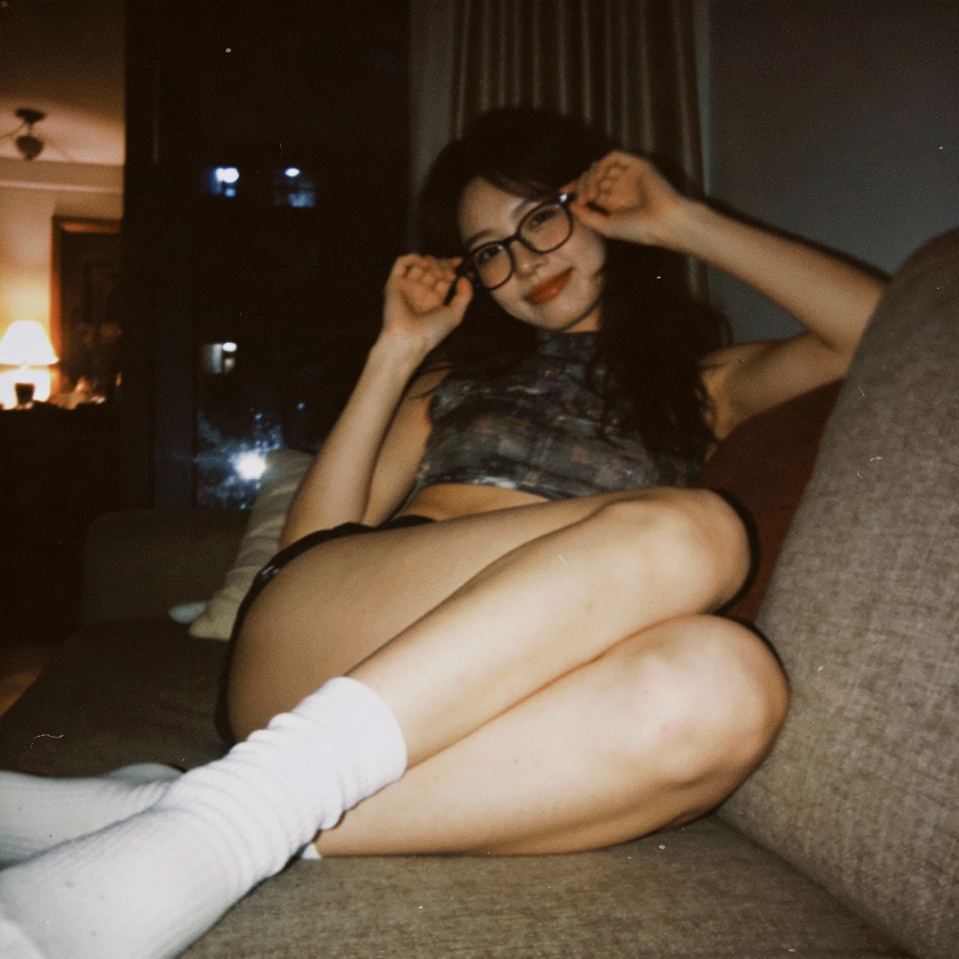 AI generated: looking at me,a sloppy snapshot. Sitting on a couch at night teasing, mini top and white socks, glas...