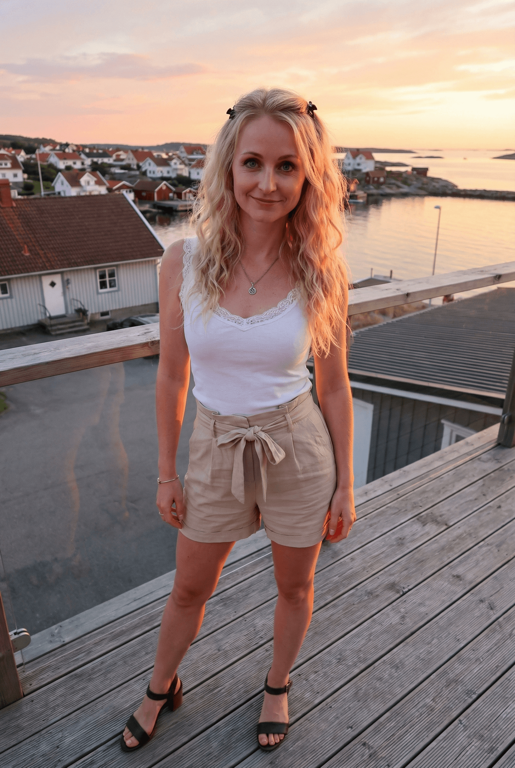 AI generated: An adult woman with a fit figure stands on a wooden deck overlooking a serene coastal town during su...
