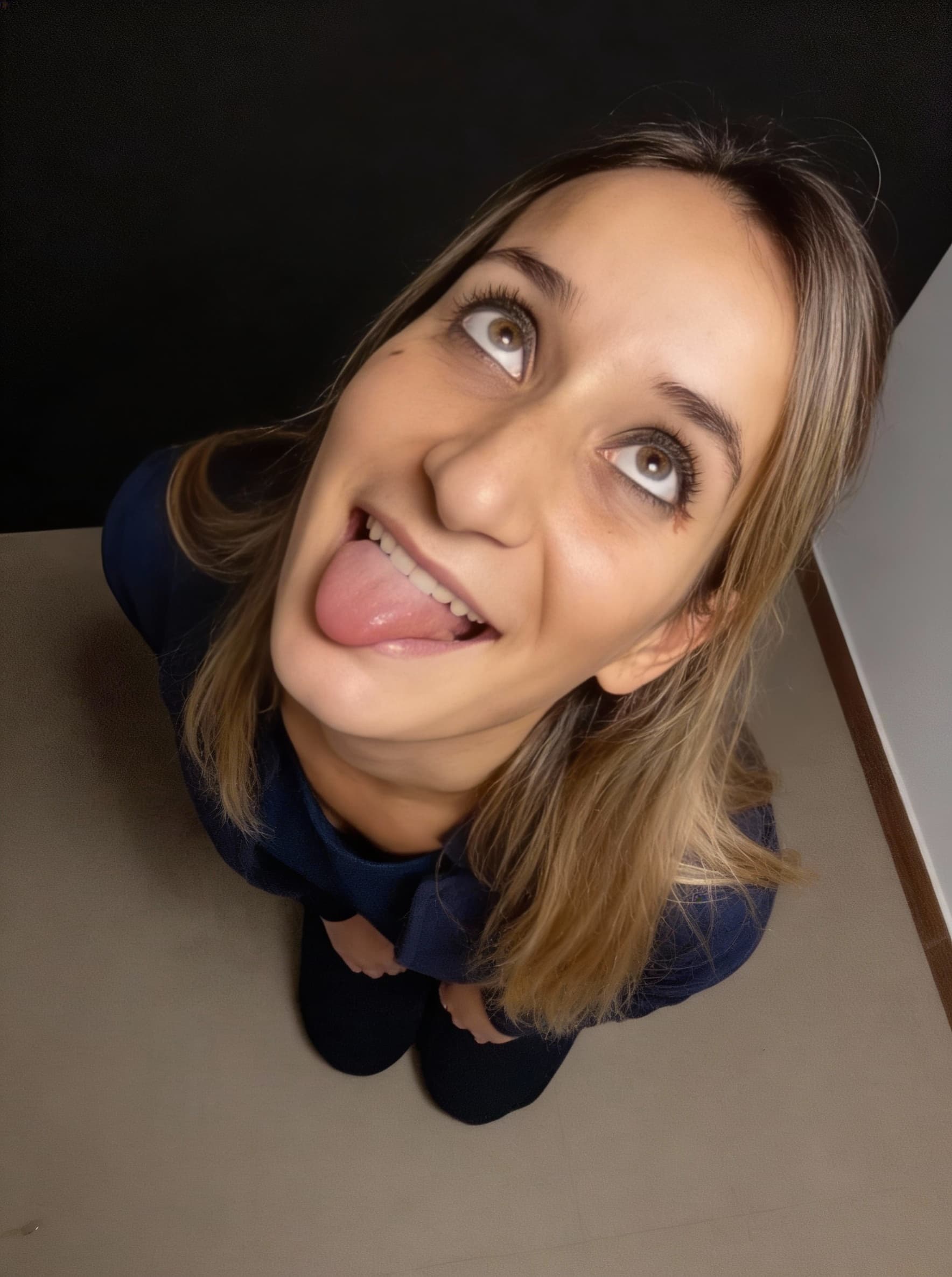 AI generated: selfie taken from a high overhead angle. kneels low, tilting her head back playfully with her tongue...
