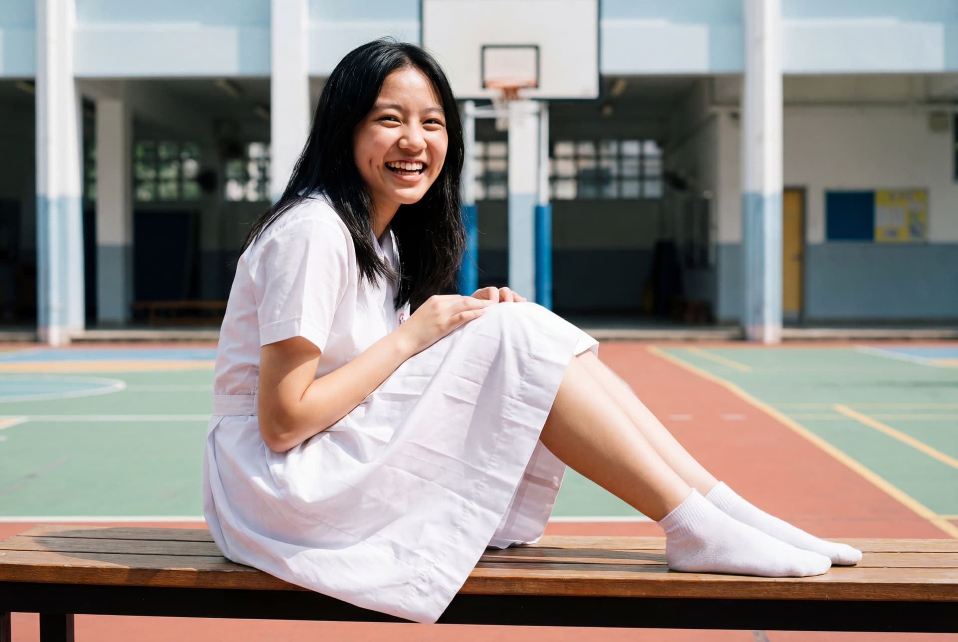 AI generated: 19歲香港女生,皮膚白晢.穿著全白色夏季中學校服短裙,文靜可愛甜美臉孔.大眼睛.有酒窩.黑髮.側拍全身照.自然細緻皮膚.不要過度柔化皮膚.坐在操場椅子.大腿偏瘦.望鏡頭大笑.真實照片.8K UHD.到...