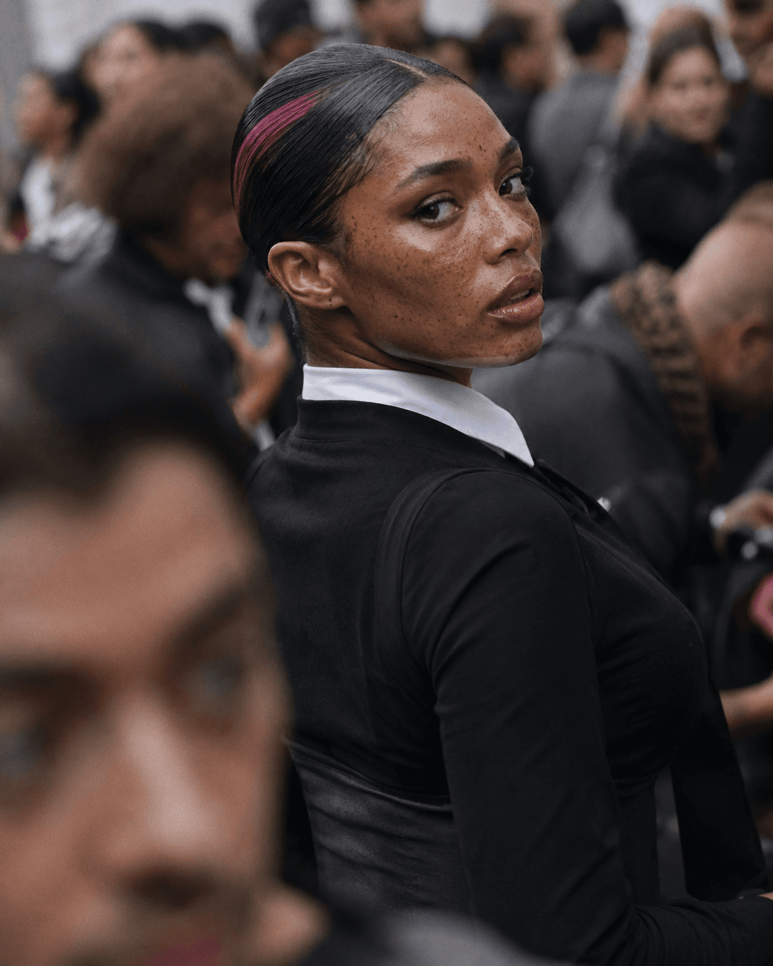AI generated: candid street-fashion portrait in a dense crowd, subject caught mid-turn while looking back toward t...