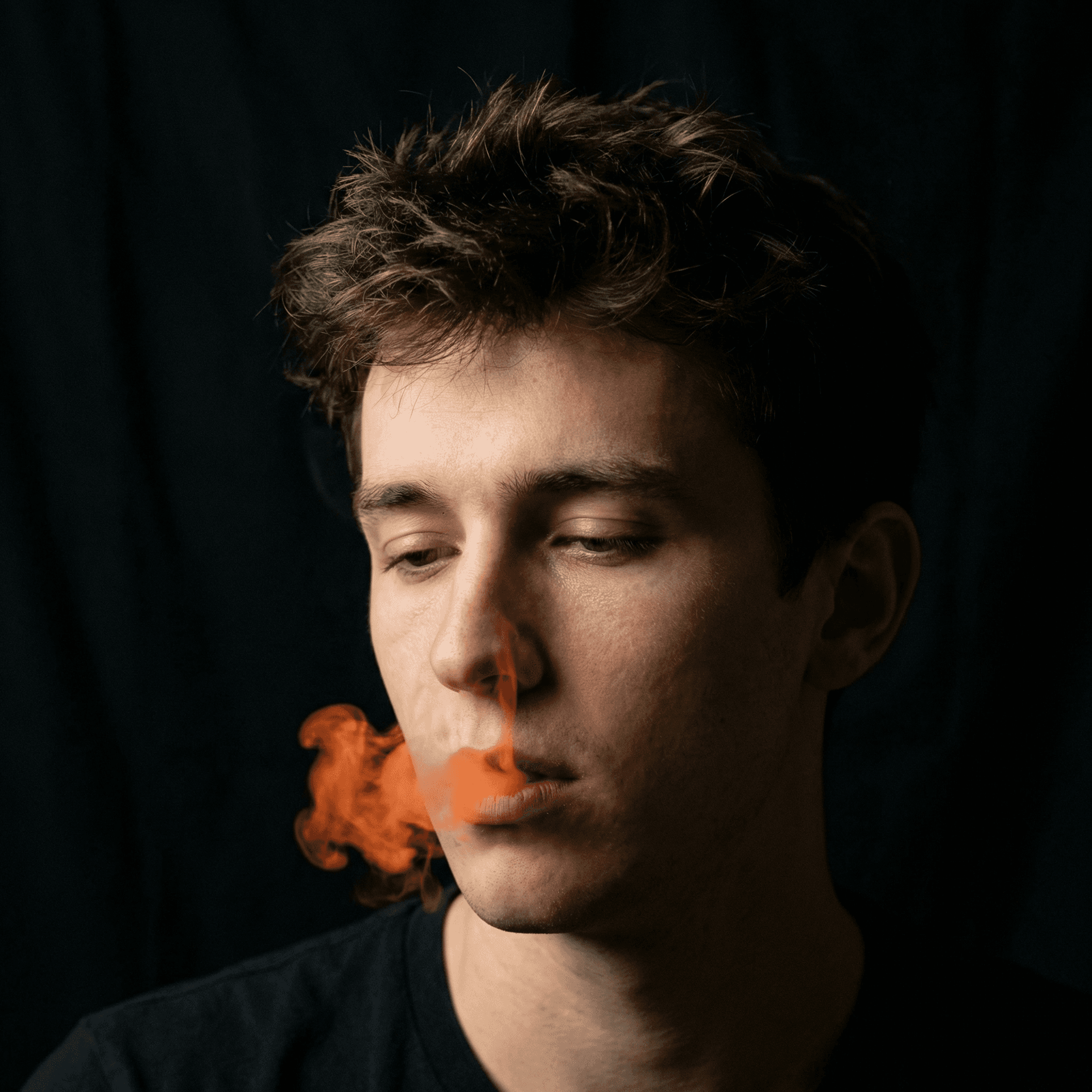 AI generated: cinematic close-up of a young man with vibrant orange smoke curling from his lips against a solid bl...