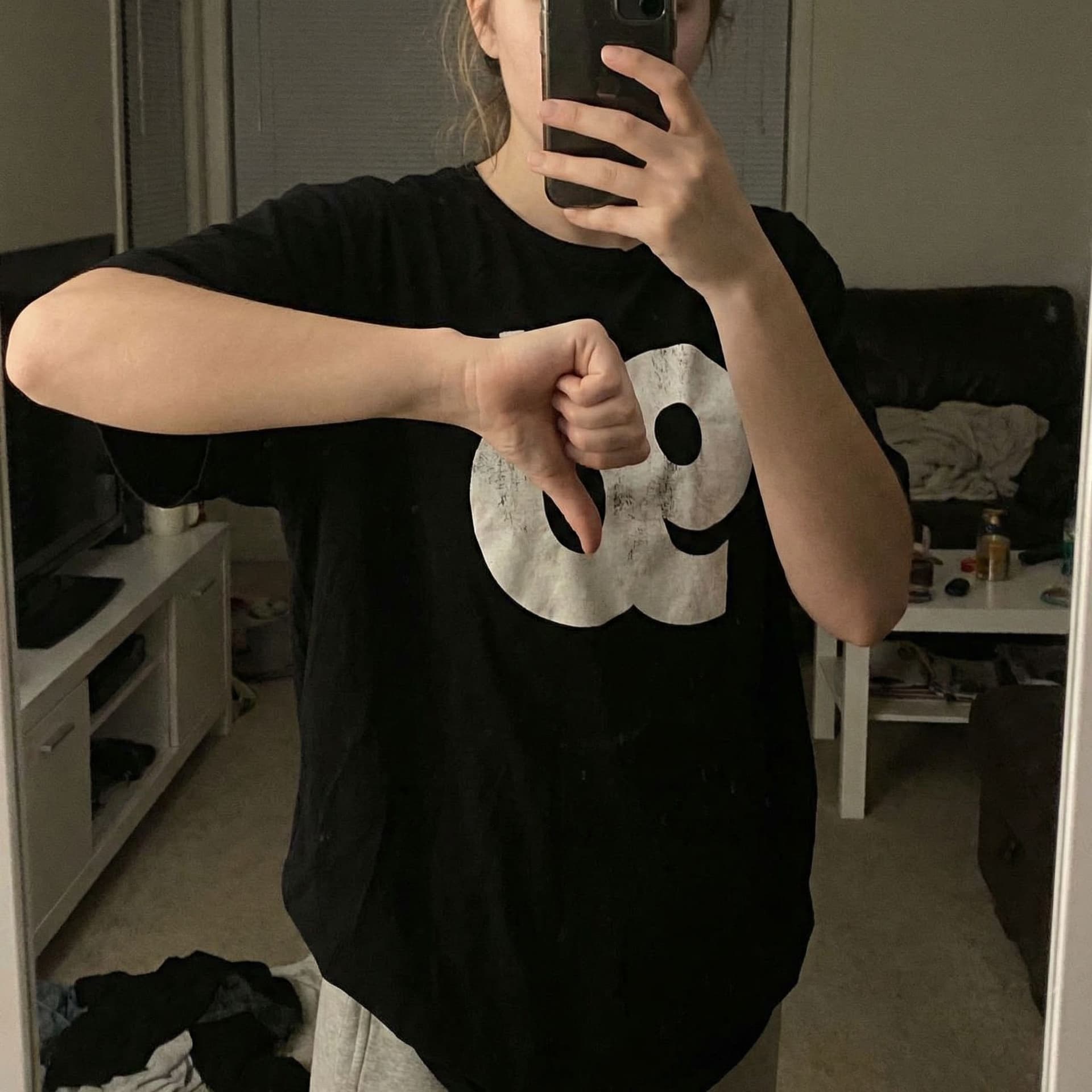 AI generated: A girl wearing a black t-shirt with a prominent, white chest takes a selfie, placing her hand on her...