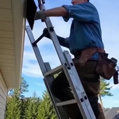 AI generated video: A realistic smartphone video of a man repairing the roof of a house while standing on a ladder. He’s...
