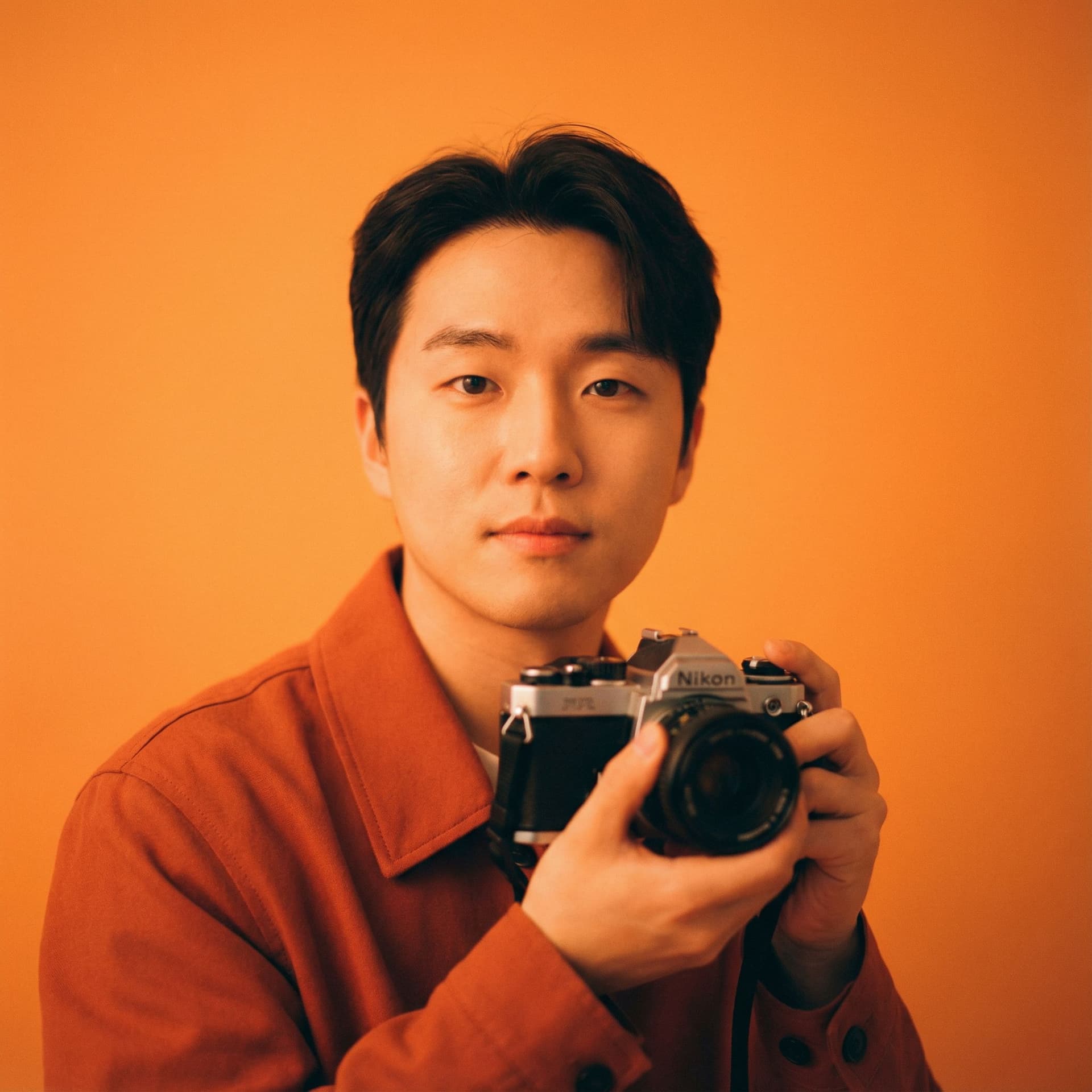 AI generated: photography, orange hue, korean man model, solid orange backdrop, using a camera setup that mimics a...