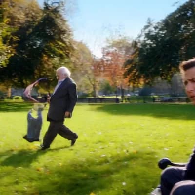 AI generated video: (Seconds 1-2) A man sits in a park, watching an old man struggling to pick up a hat that has been bl...
