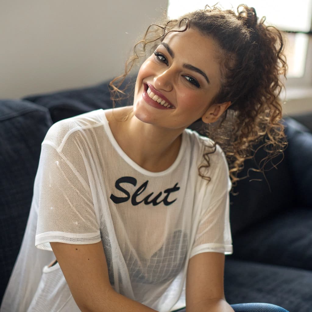 AI generated: A Albanian woman with curly hair pulled into a half-up style smiles warmly at the camera. She wears ...