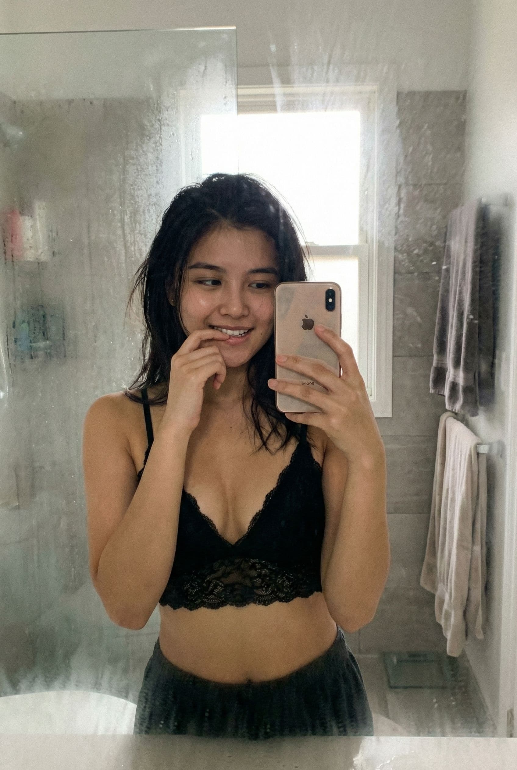 AI generated: Casual mirror selfie in a bathroom, smartphone photo quality. Slim brunette adult with a playful exp...