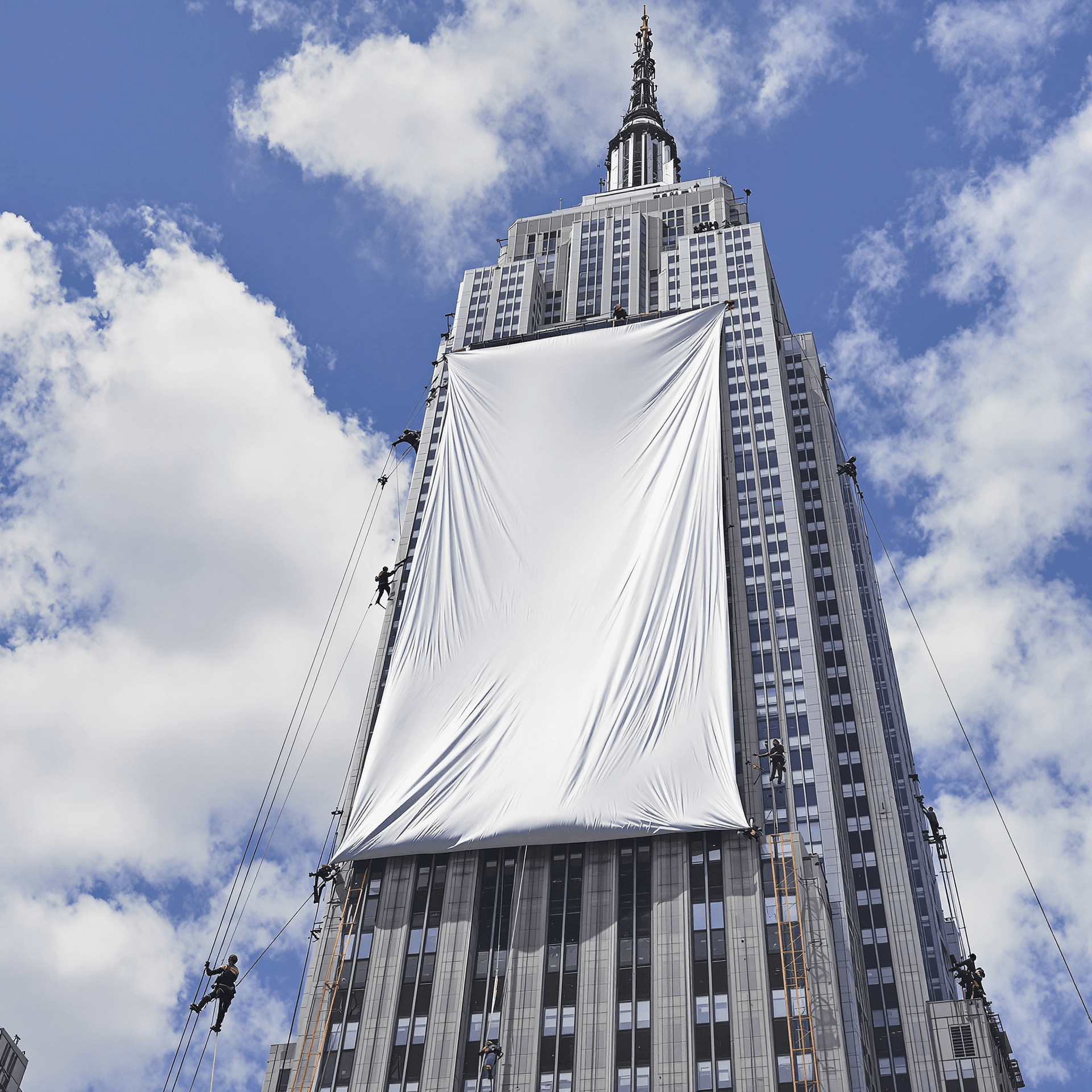 AI generated: The iconic Empire State Building in New York City, with a team of workers carefully installing a mas...